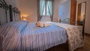Un dormitorio con cama, armario, ventana con cortinas y lámpara.