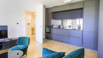 Une cuisine moderne avec des meubles gris et un four encastré. On y trouve un fauteuil turquoise et une petite table avec un plateau noir.