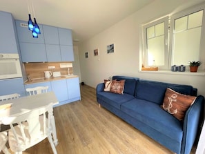 Ein gemütlicher Wohnraum mit Küchenzeile, einem blauen Sofa und einem Esstisch.