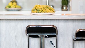 A kitchen counter with a fruit bowl, a sink, and two bar stools.