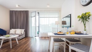 Una sala moderna con un sofá, una mesa de comedor con sillas, una mesa de centro, un televisor y un reloj en la pared.