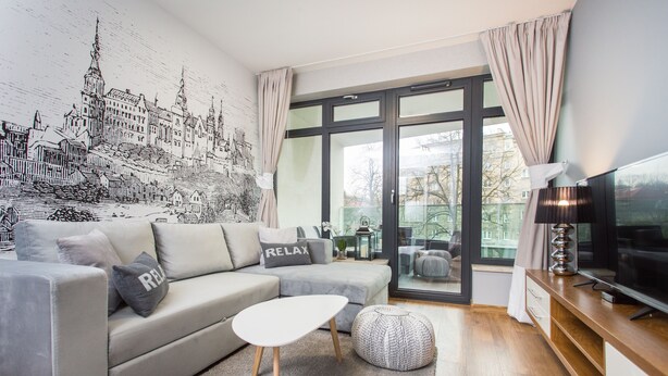 Una sala de estar moderna con un sofá gris, una mesita de centro blanca y un amplio ventanal con cortinas.