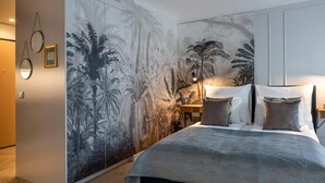 Un dormitorio con un gran mural de follaje tropical en la pared, una cama con colcha estampada en gris y una mesita de noche con lámparas.