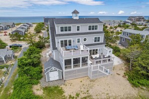 A two-story beachfront house with a covered patio, a small tower, and a view of the ocean. - Bright & Beautiful Waterfront Cape Cod Home (Sandwich)