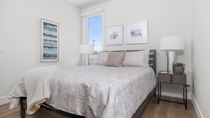 A bedroom with a bed, bedside tables, a window, and wall art. - Wake Up to Bay Views | Walk Downtown + Beach (Traverse City)