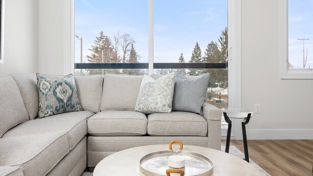 A modern living room with a sectional sofa, a round coffee table, and a view through large windows. - Wake Up to Bay Views | Walk Downtown + Beach (Traverse City)