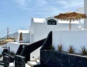 Un bâtiment blanc avec un escalier en pierre, une petite fenêtre et un parasol en paille.