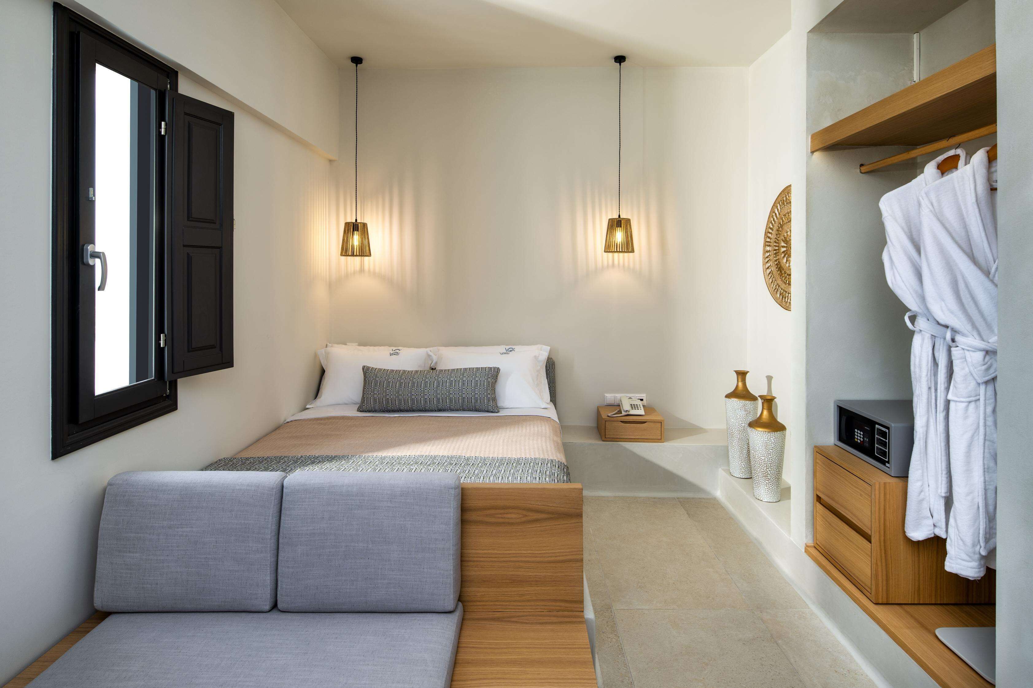 Une chambre à coucher moderne avec un lit, des tables de chevet, une petite table et un peignoir suspendu à un porte-manteau.