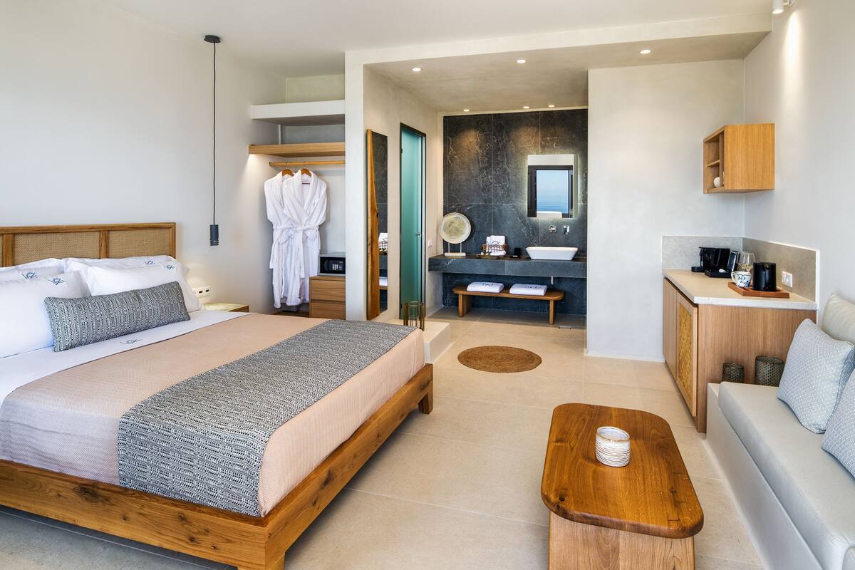 Een moderne hotelkamer met een groot bed, een zithoek, een kitchenette en een badkamer met een grote spiegel.