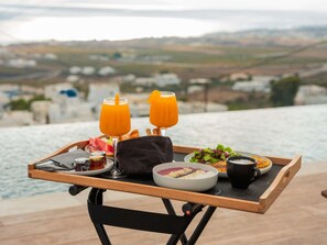 Un plateau de petit-déjeuner avec du jus d’orange, du pain, un saladier de salade et une tasse de café, posé sur un balcon donnant sur un paysage magnifique.