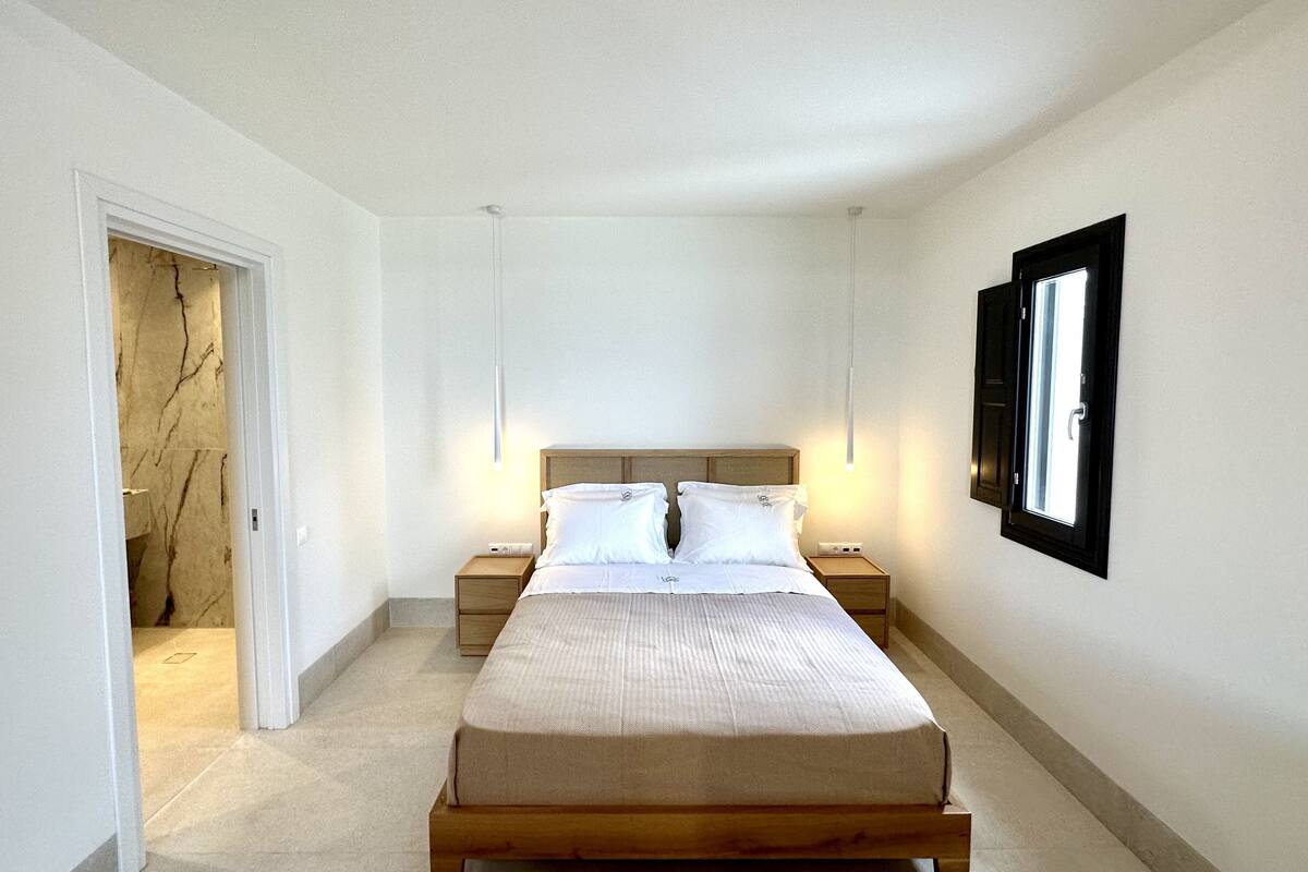Een slaapkamer met een bed, nachtkastjes, een deur en een aan de muur hangend schilderij.