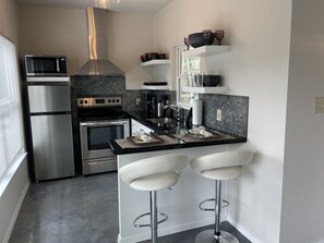 Uma cozinha moderna com eletrodomésticos de aço inoxidável, bancada preta e dois banquetes brancos.