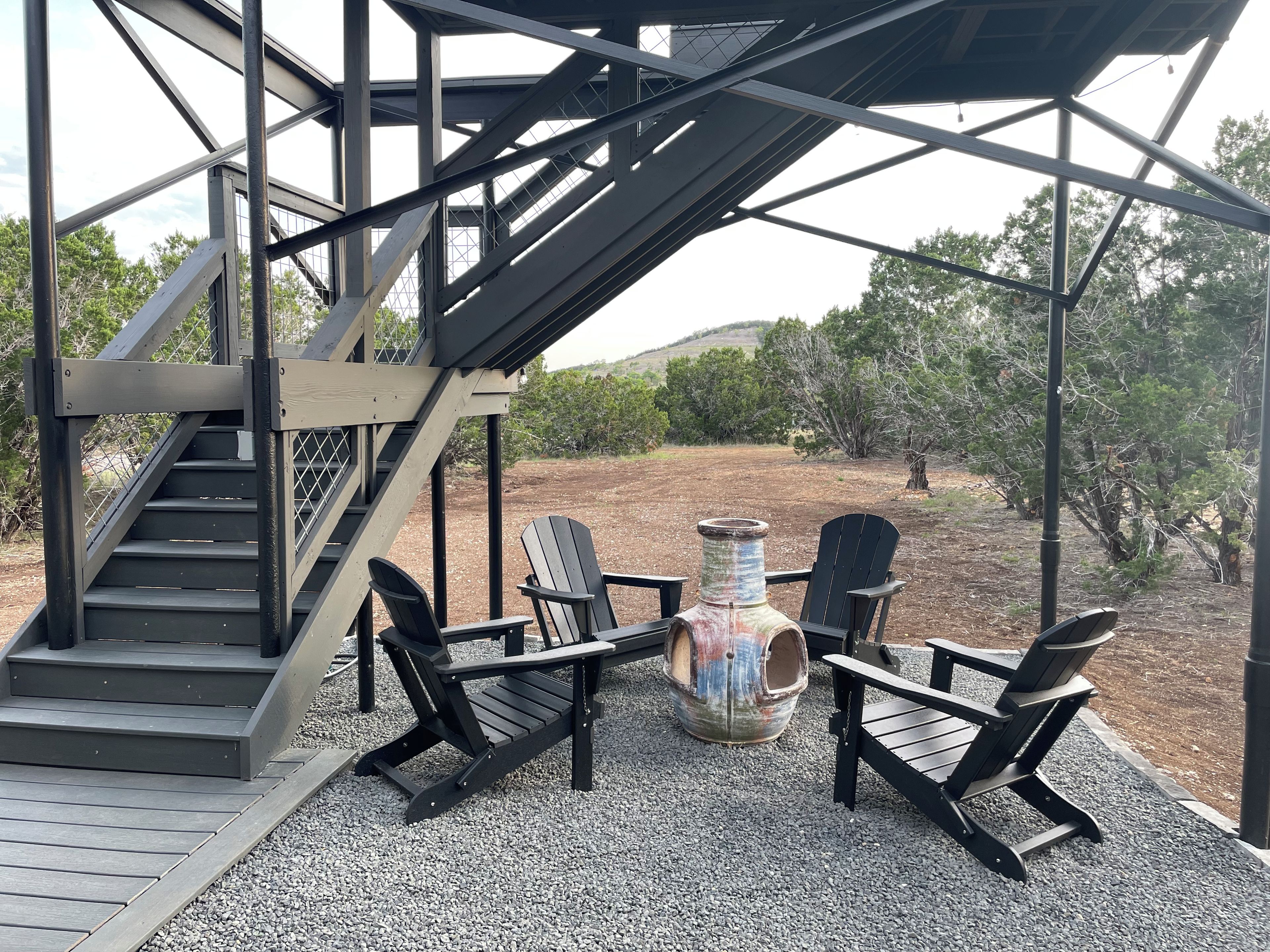 Un espace extérieur abrité, doté d’un escalier, de deux fauteuils Adirondack et d’une table rustique.