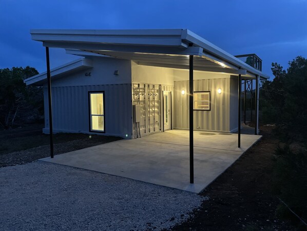 Uma casa moderna com varanda coberta, porta de entrada de vidro e banheiro visível.