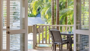 Un balcon avec une table et des chaises, donnant sur une piscine et des palmiers.