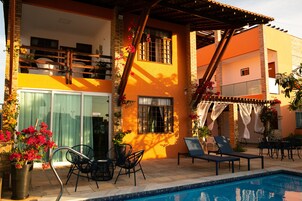 Un edificio de dos pisos con piscina, mobiliario exterior y un patio cubierto.