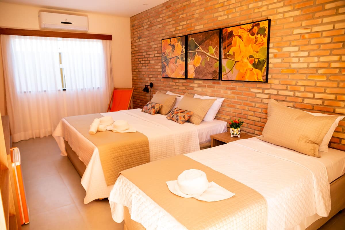 A hotel room with two beds, a brick wall, and a large window with curtains.