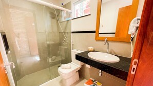 A bathroom with a glass-enclosed shower, a white toilet, a sink with a black countertop, and a mirror above the sink. - Pousada das Flores (Luis Correia)