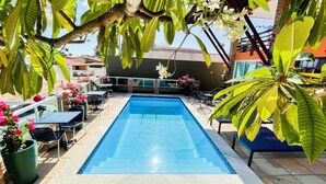 A rectangular swimming pool with a tiled edge, surrounded by outdoor furniture and potted plants. - Pousada das Flores (Luis Correia)