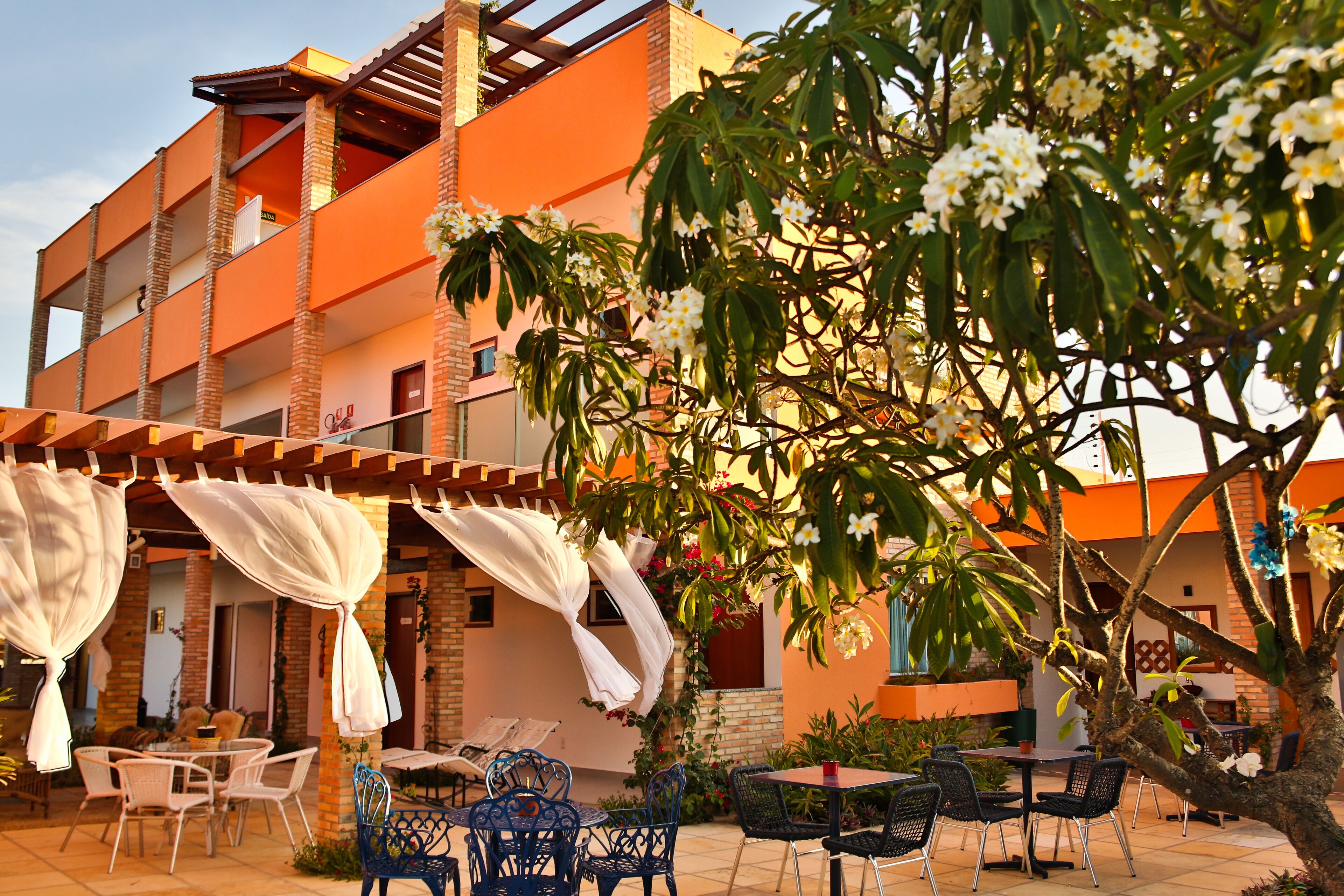 An outdoor patio area with tables and chairs, surrounded by a building with orange walls and a brick facade.