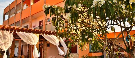 An outdoor patio area with tables and chairs, surrounded by a building with orange walls and a brick facade.