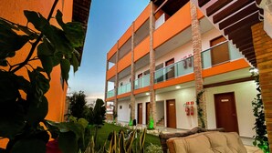 A multi-story hotel with balconies, a well-maintained garden, and a seating area with a chair. - Pousada das Flores (Luis Correia)
