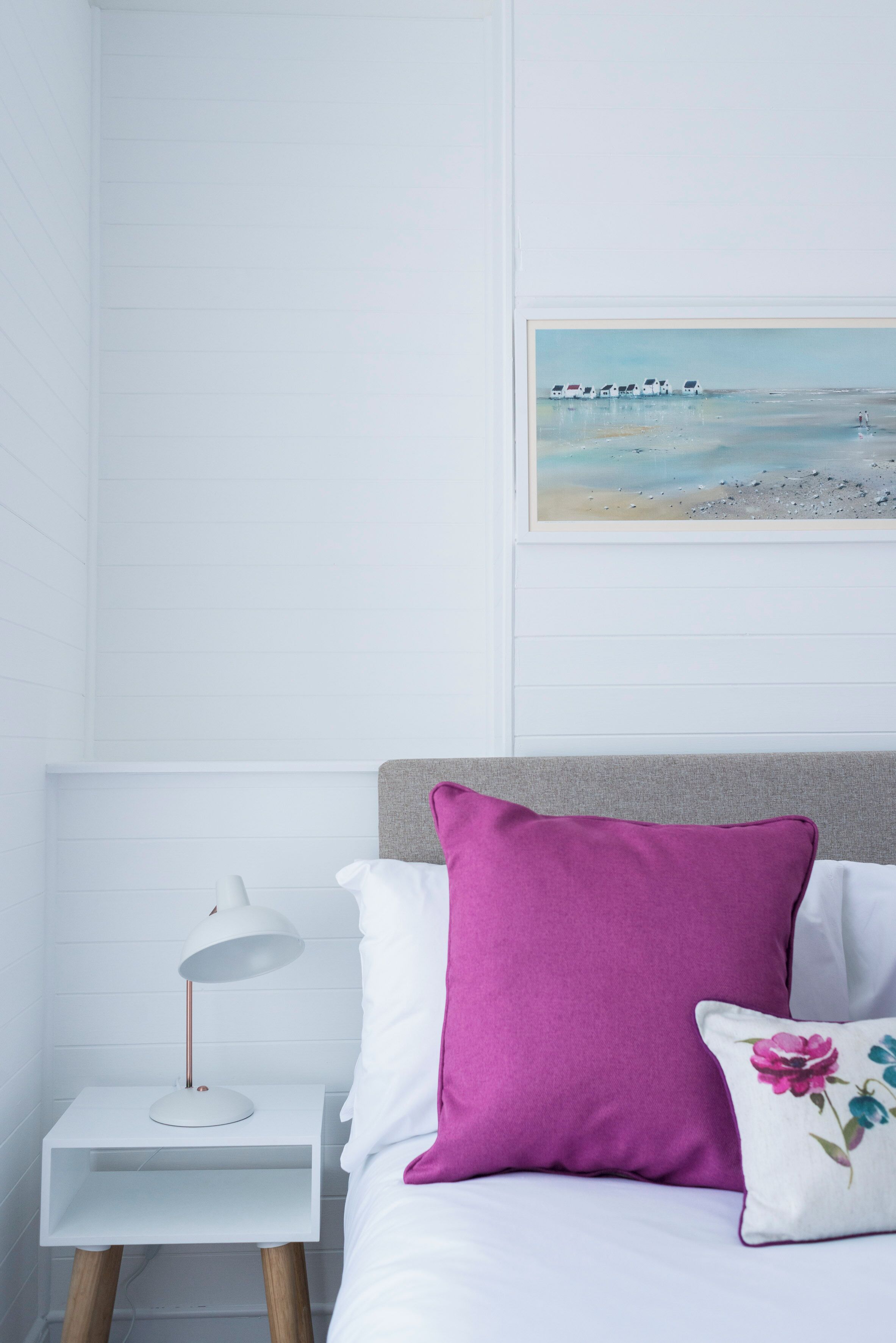 A neatly arranged bedroom with a bed, a nightstand with a lamp, and a framed picture on the wall.