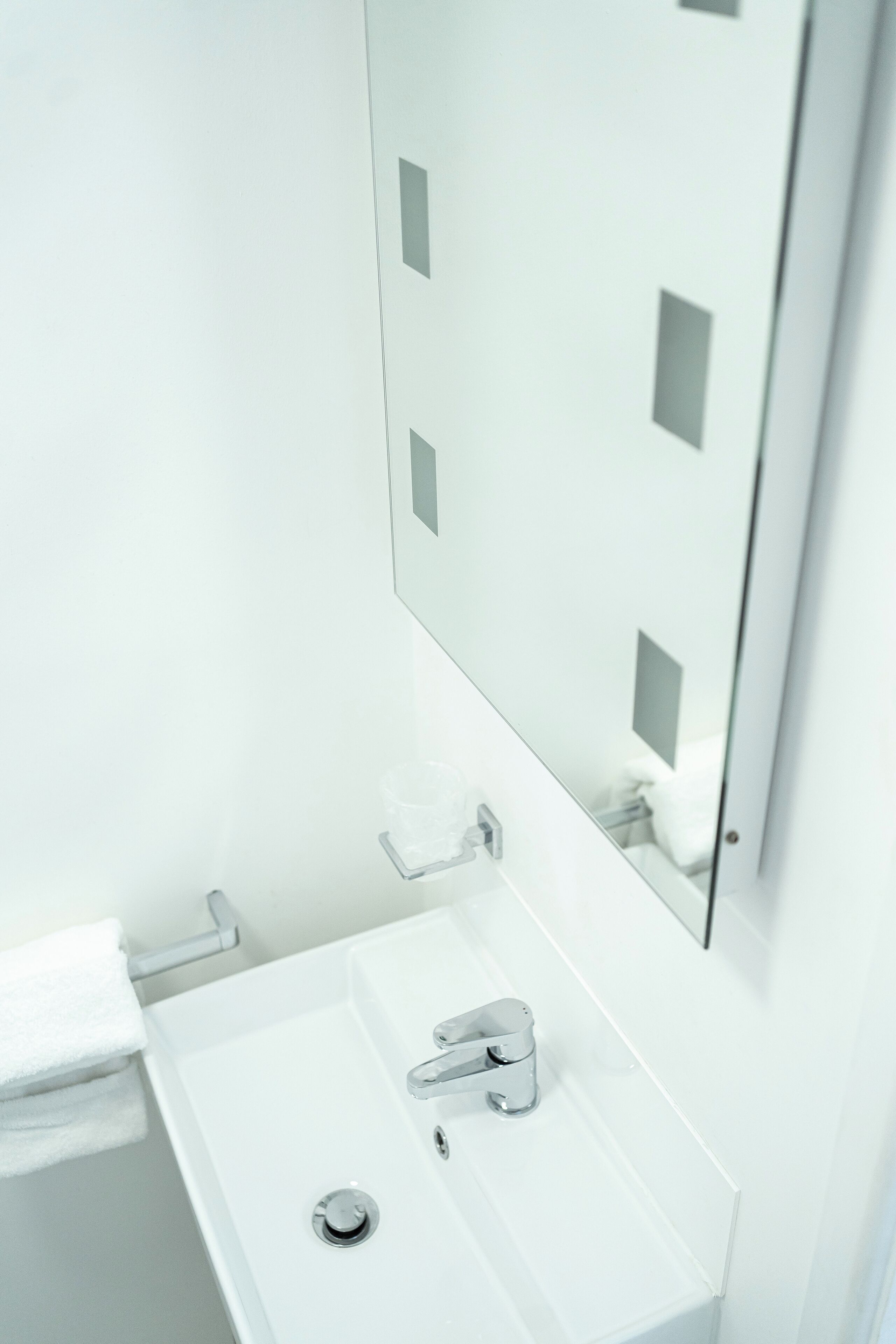 Une salle de bain blanche avec un lavabo, un miroir et un porte-serviettes.