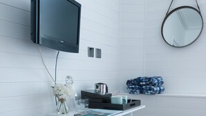 Une pièce moderne aux murs recouverts de panneaux blancs, comprenant un bureau, un téléviseur à écran plat, un miroir et un petit coin salon.