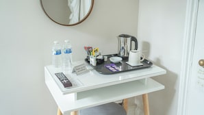 Sur le bureau d’une chambre d’hôtel, on trouve un plateau avec une cafetière, des tasses et des en-cas. Deux bouteilles d’eau et une télécommande sont également posées sur le bureau.