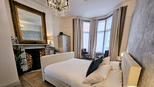 Une chambre spacieuse avec un grand lit, un lustre, une cheminée et une vue sur l’extérieur.