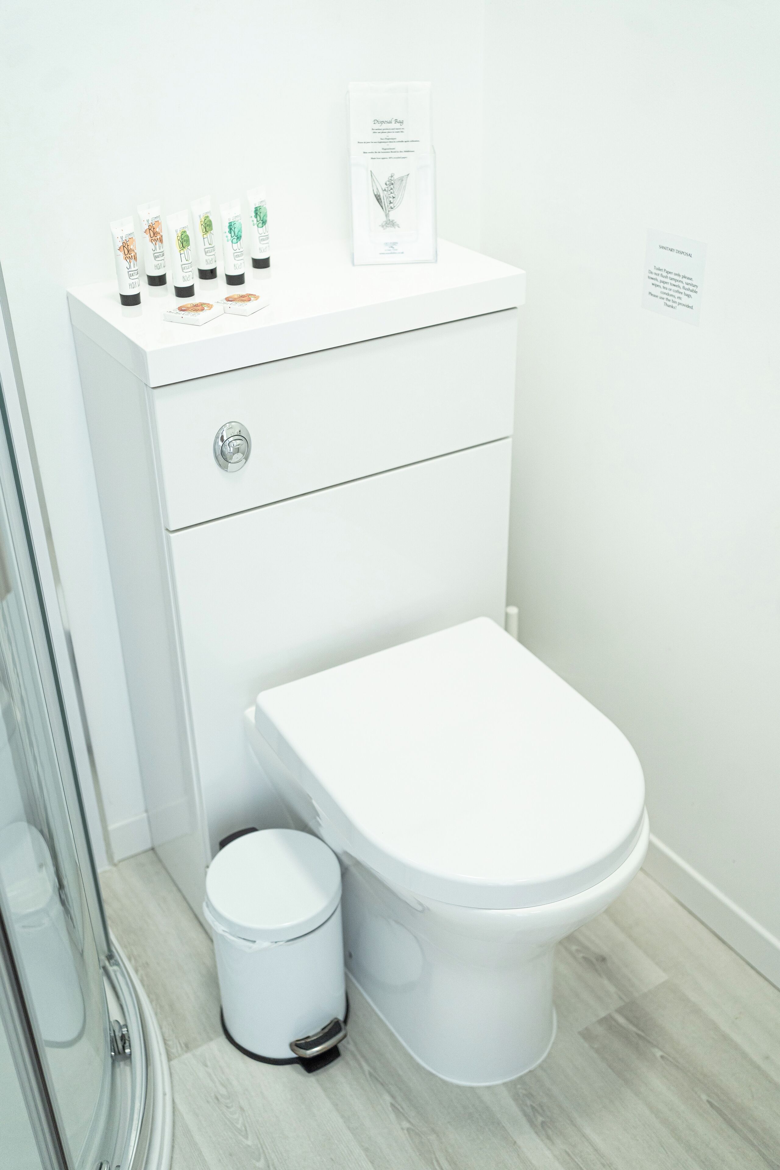 A modern bathroom with a white toilet, a small trash bin, and a glass shower enclosure.