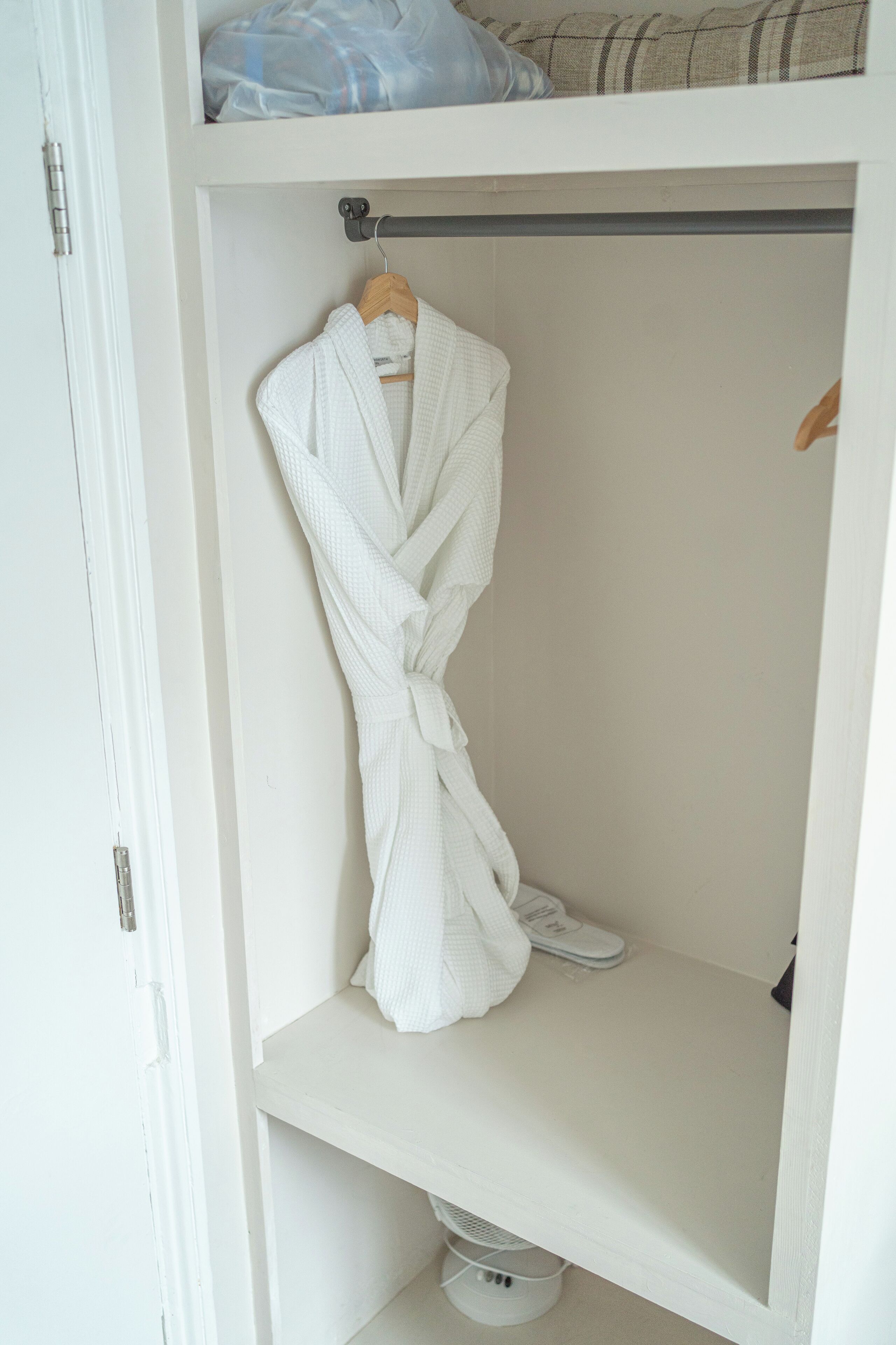 A white closet with a robe hanging on a rod and a pair of shoes on the lower shelf.