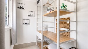 A room with white walls, a window with curtains, and a white shelving unit with wooden shelves. - A Wave from it All- Escape to Paradise (Berrara)