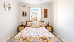 A bedroom with a bed, two nightstands, a round mirror, and artwork on the walls.