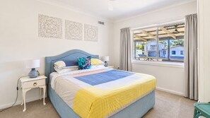 A bedroom with a bed, two bedside tables, a window with curtains, and decorative wall art.