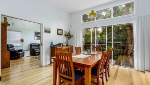 A dining area with a wooden table and chairs, a coffee machine, and a view of the outdoors through large windows. - The Yellow Door Inverloch (Inverloch)