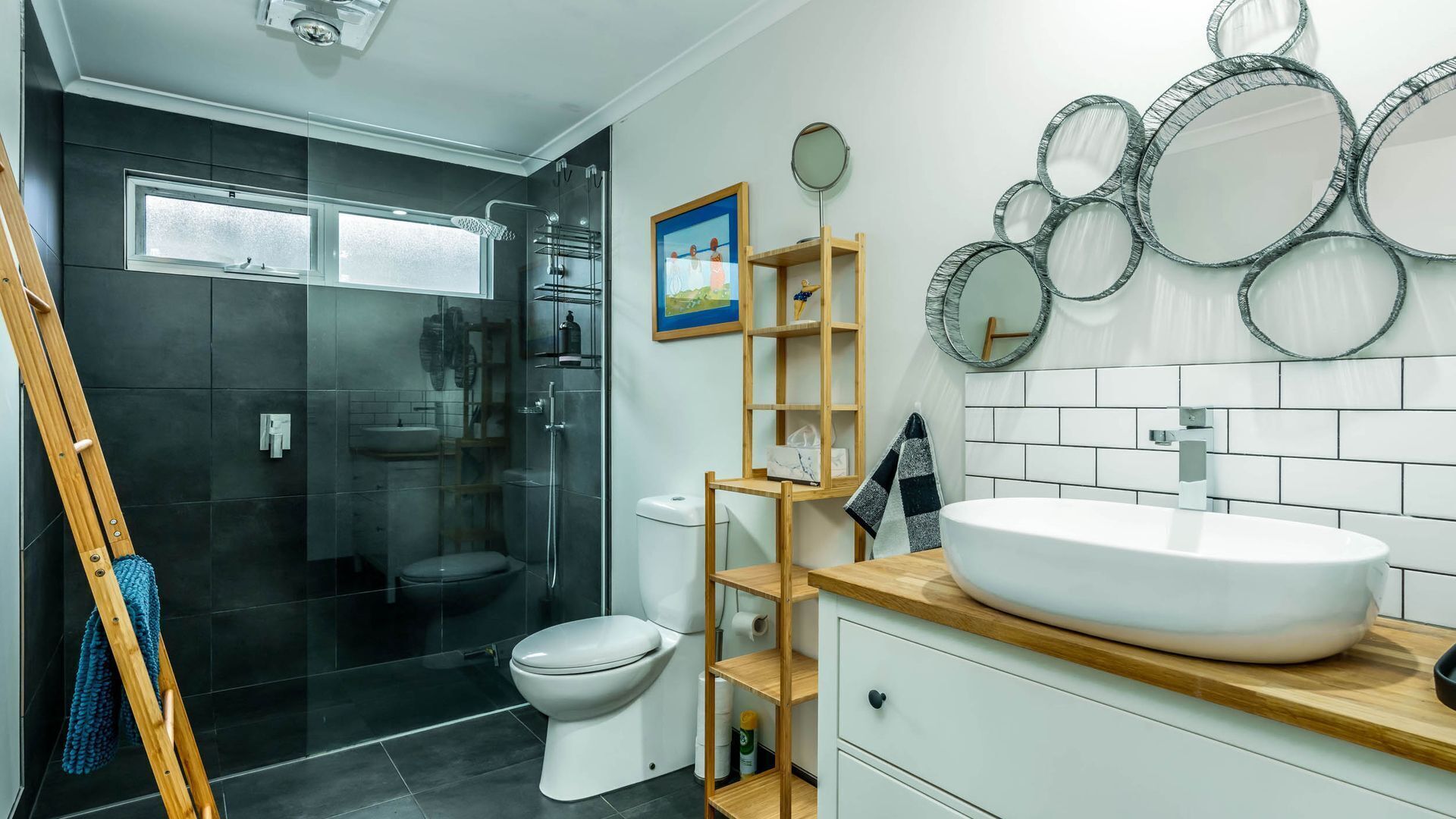 Un baño moderno con cabina de ducha de vidrio, inodoro blanco, tocador de madera con un lavamanos grande y estante de madera.