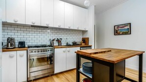 A modern kitchen with white cabinets, a wooden countertop, stainless steel appliances, and a wooden dining table. - The Yellow Door Inverloch (Inverloch)