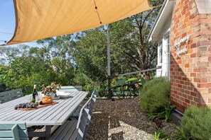 Un patio con una mesa de madera lista para comer, una botella de vino y un pan.