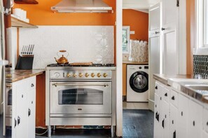Une cuisine équipée d’une cuisinière en acier inoxydable, d’un lave-linge et de meubles blancs.