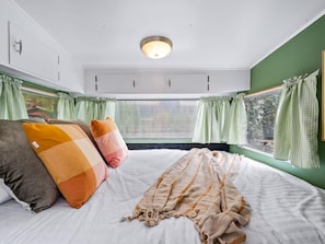 Un dormitorio con cama, almohadas, una colcha, una ventana con cortinas y una lámpara en el techo.