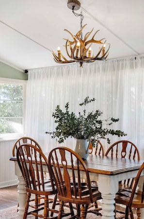 A dining area with a wooden table and chairs, a chandelier, and a potted plant. - Luxe Farm Stay: Animals, Fire Pit, Beach (Wamberal)