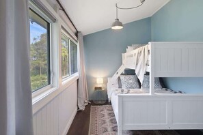 A bedroom with a bunk bed, a bedside lamp, and a view of the outdoors through large windows.