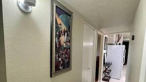 Un couloir avec un tapis à motifs, une œuvre d’art encadrée et un luminaire.