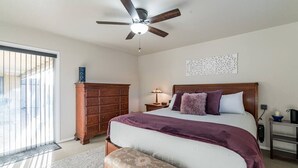 Une chambre à coucher avec un lit, une commode en bois, une table de chevet avec une lampe et un ventilateur de plafond.