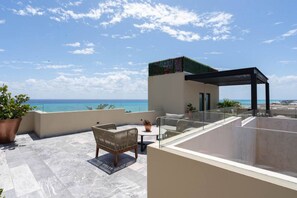 A rooftop terrace with a view of the ocean, a seating area with a table, and a small garden.