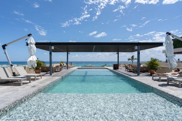 A pool area with lounge chairs and umbrellas, overlooking a clear blue sky and ocean.