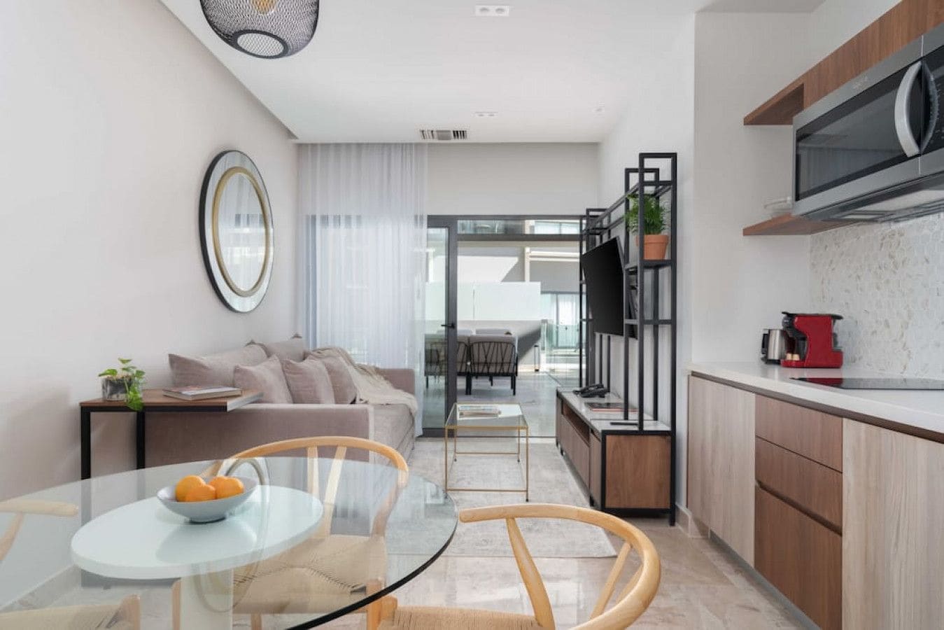 Cozinha moderna com micro-ondas, máquina de café e área de jantar com mesa e cadeiras de vidro.