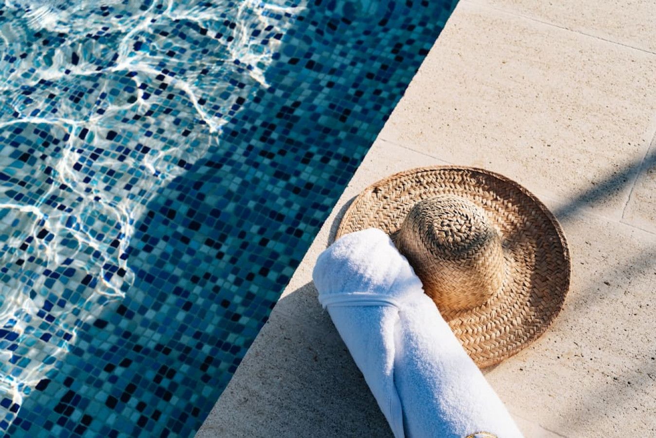 Une scène de bord de piscine avec un chapeau de paille tressé et une serviette blanche.